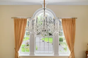 This image shows a large Chandelier framed by an imposing Adams style window looking down a tree lined avenue.
